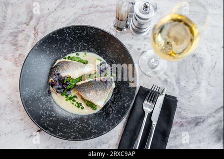 Bar en sauce crème avec épinards et huile verte sur une assiette blanche Banque D'Images