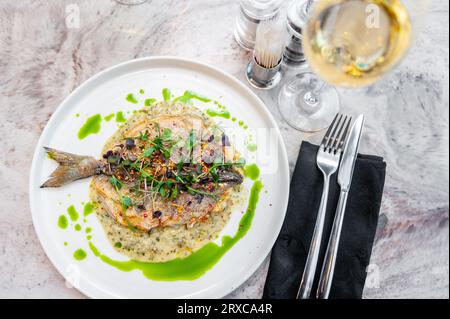 Bar en sauce crème aux herbes provençales et huile verte sur une assiette blanche Banque D'Images