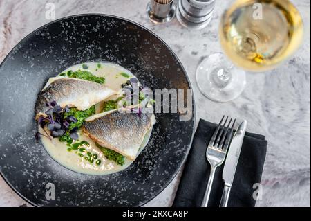 Bar en sauce crème avec épinards et huile verte sur une assiette blanche Banque D'Images