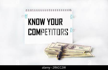 Bloc-notes avec le texte CONNAÎTRE VOS CONCURRENTS, stylo, dollars sur un fond blanc. Concept commercial. Banque D'Images