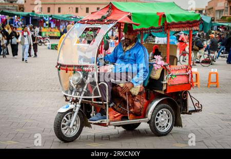 Marrakech, Maroc, 8 avril 2023. Vue latérale de face d'un mâle marocain conduisant lentement un tuk tuk sur la place Marrakech Jemaa el-Fnaa. Banque D'Images