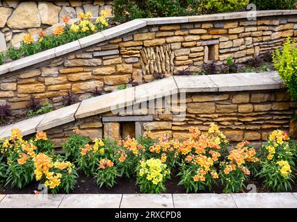Aménagement paysager avec murs de soutènement et parterres de fleurs dans l'arrière-cour de la maison, aménagement paysager de jardin haut de gamme avec des murs de pierre en été. Fleurs et pla Banque D'Images