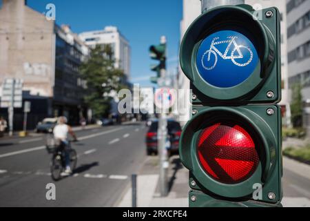 Mise au point sélective, feux de circulation avec symbole de vélo sur le trottoir à côté de la piste cyclable en Europe et défocalisation des gens en vélo. Banque D'Images