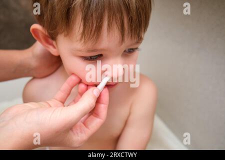 La maman maintient l'hygiène en nettoyant le nez de son bébé fils avec un coton dans la salle de bain. Enfant âgé de deux ans (garçon de deux ans) Banque D'Images