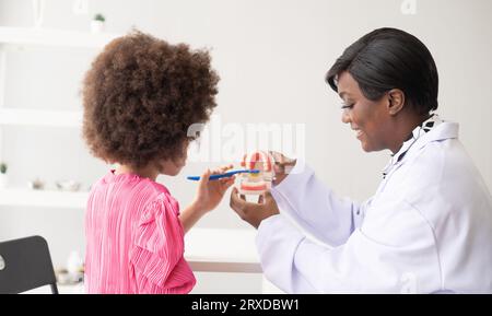 Dentiste afro-américain expliquant à un enfant afro métis comment se brosser les dents. Le médecin et le concept de santé de l'enfant. Banque D'Images