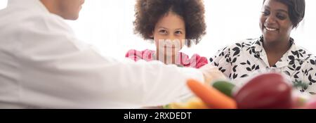 Médecin nutritionniste hispanique consultant un enfant métis avec sa mère afro-américaine au sujet d'une nutrition. Nourriture de légumes - une nouvelle façon pour le bien Banque D'Images