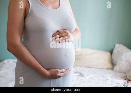 Une jeune femme enceinte avec un gros ventre en vêtements décontractés caresse son ventre. Banque D'Images