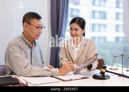 Homme d'affaires senior signant le contrat sur tablette tandis que l'avocate femme explique la durée et l'accord juridique. Banque D'Images