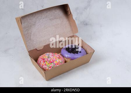 Délicieux beignets sucrés avec différentes saveurs dans une petite boîte en papier. Image isolée sur fond blanc Banque D'Images