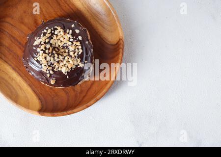 Vue de dessus plat de délicieux beignet glacé au chocolat sucré avec noix de cajou servi sur une assiette en bois. Image isolée sur fond blanc Banque D'Images