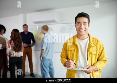 Portrait de startupper souriant prenant des notes dans le document sur le presse-papiers Banque D'Images