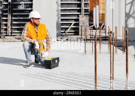 Ouvrier réparateur en uniforme et casque travaillant avec un tournevis sans fil et une boîte à outils. Banque D'Images