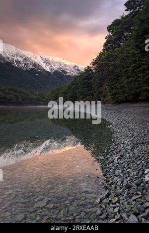 Coucher de soleil reflété dans North Lake avec des montagnes enneigées et la forêt indigène. Lacs Mavora, Île du Sud, Nouvelle-Zélande Banque D'Images