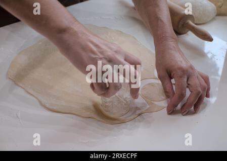 Mains d'une femme en train de faire de petits rouds de pâte avec un verre. Préparation du vareniki. Banque D'Images