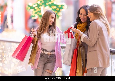 Trois belles filles regardent leurs cadeaux de Noël achetés dans le centre commercial. Banque D'Images