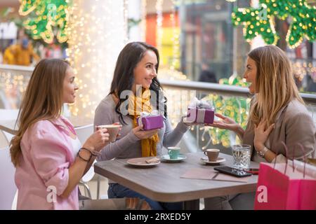 Trois belles femmes sont assises dans un café dans un centre commercial, distribuant des cadeaux de Noël. Banque D'Images