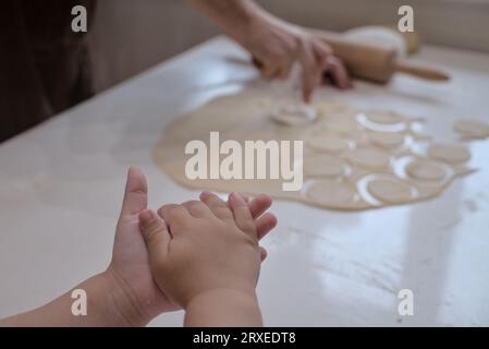 Les mains des petits enfants tenant la pâte pendant que la femme adulte prépare la nourriture en arrière-plan. Banque D'Images