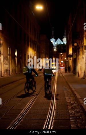 Deux livreurs de nourriture font du vélo dans la ville nocturne. Banque D'Images