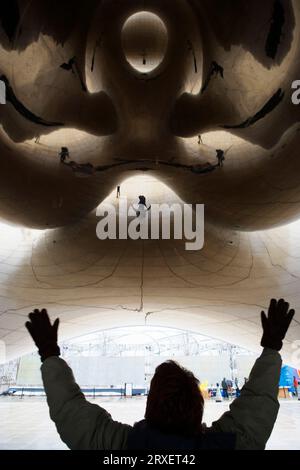 Vue arrière d'une personne avec les bras levés avec des reflets dans la sculpture Cloud Gate, Chicago, il. Banque D'Images