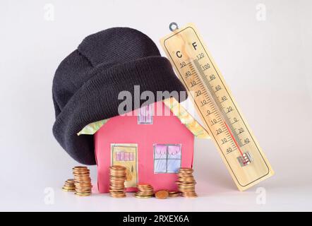 Maison modèle avec chapeau d'hiver, piles d'argent et thermomètre.augmentation des coûts de chauffage, isolation thermique et les prix de l'énergie en raison de la pénurie de gaz de chauffage, Banque D'Images