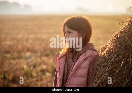 Mignonne adolescente dans le champ avec des coupures de blé et des meules de foin. matin, brouillard Banque D'Images