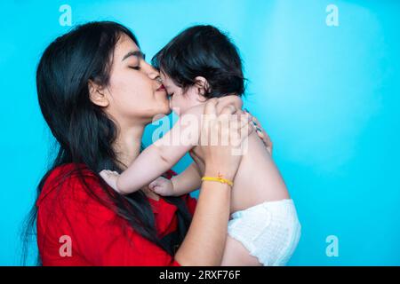 Fille adolescente indienne jouant six mois mignon petit bébé en couche isolé sur fond bleu. Enfant et sœur asiatiques, famille heureuse. Banque D'Images