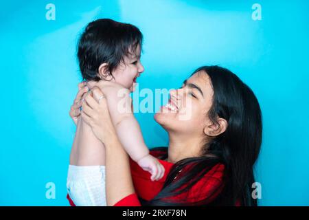 Fille adolescente indienne jouant six mois mignon petit bébé en couche isolé sur fond bleu. Enfant et sœur asiatiques, famille heureuse. Banque D'Images