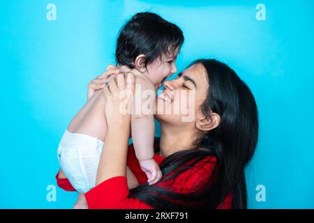 Fille adolescente indienne jouant six mois mignon petit bébé en couche isolé sur fond bleu. Enfant et sœur asiatiques, famille heureuse. Banque D'Images