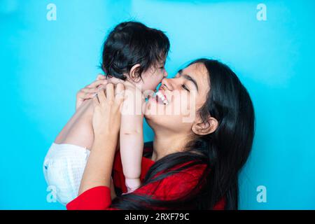 Fille adolescente indienne jouant six mois mignon petit bébé en couche isolé sur fond bleu. Enfant et sœur asiatiques, famille heureuse. Banque D'Images