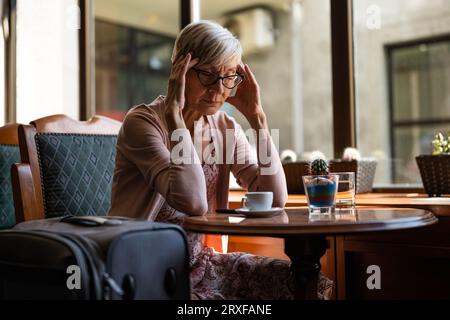 Femme mature est assise dans un café à l'aéroport, attendant l'embarquement. Banque D'Images