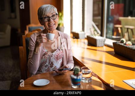 Femme mature est assise dans le café et relaxant. Banque D'Images