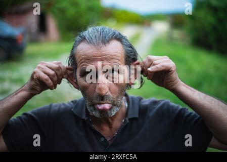 En plein air, un joyeux homme de 60 ans, arborant des lunettes et de longues serrures, avec l'héritage serbe, partage des conversations animées tout en jouant Banque D'Images