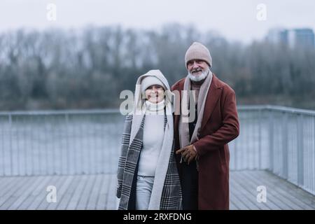 Élégant couple senior marchant près de la rivière, pendant la journée froide d'hiver. Banque D'Images