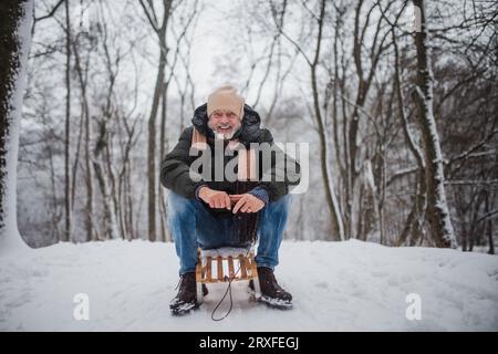 Homme senior s'amusant pendant la journée froide d'hiver, en traînant en traîneau sur la colline. Banque D'Images