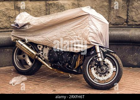 Moto couverte. Moto garée dans une toile de protection, étui. La moto recouverte d'une toile cirée d'une pluie. Parking étanche à l'extérieur du Banque D'Images