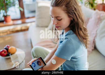 Femme diabétique vérifiant le taux de glucose sanguin à la maison à l'aide d'un moniteur de glucose continu. Banque D'Images