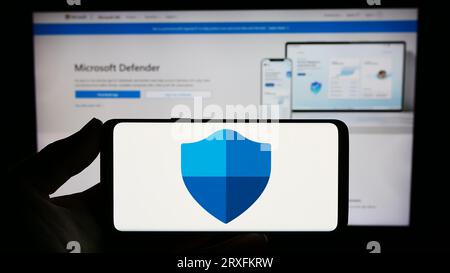 Personne tenant smartphone avec le logo du logiciel de sécurité Microsoft Defender antivirus sur l'écran en face du site Web. Concentrez-vous sur l'affichage du téléphone. Banque D'Images