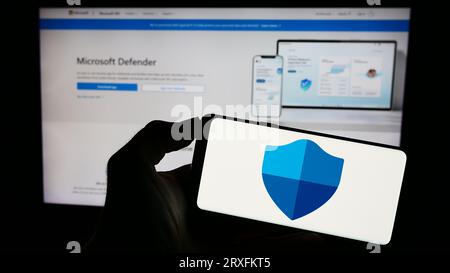 Personne tenant le téléphone mobile avec le logo du logiciel de sécurité Microsoft Defender antivirus sur l'écran en face de la page Web. Concentrez-vous sur l'affichage du téléphone. Banque D'Images