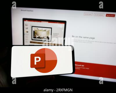 Personne tenant le téléphone portable avec le logo du logiciel de présentation Microsoft PowerPoint sur l'écran en face de la page Web de l'entreprise. Concentrez-vous sur l'affichage du téléphone. Banque D'Images