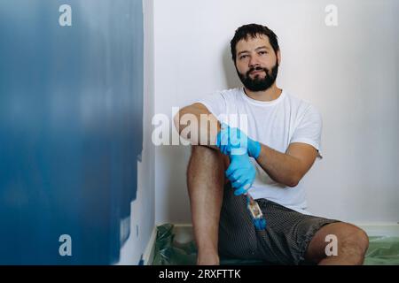 rénovation domiciliaire. Homme barbu caucasien ayant le repos après avoir peint l'image du mur avec la mise au point sélective Banque D'Images