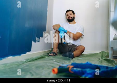 rénovation domiciliaire. Homme barbu caucasien ayant le repos après avoir peint l'image du mur avec la mise au point sélective Banque D'Images