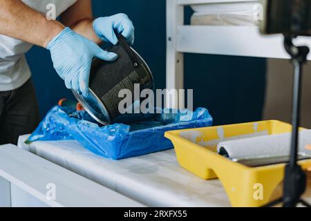 homme versant de la peinture bleue d'un bocal en métal dans un plateau Concept de maison de rénovation. Smartphone sur trépied pour enregistrer la vidéo du processus Banque D'Images
