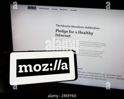 Personne tenant le téléphone mobile avec le logo de l'organisation open source Mozilla Foundation sur l'écran en face de la page Web. Concentrez-vous sur l'affichage du téléphone. Banque D'Images