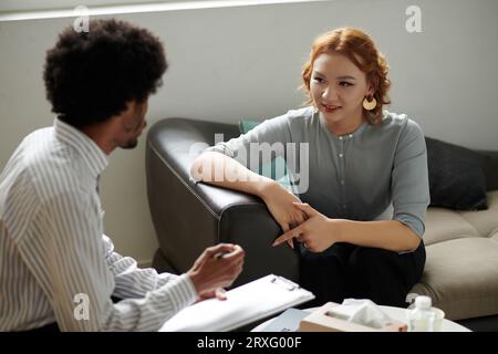 Jeune femme souriante parlant à son psychologue pendant la séance de thérapie Banque D'Images