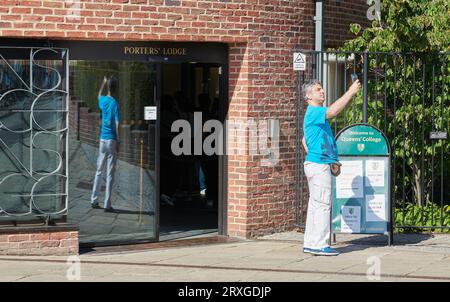 Un touriste solitaire prend un selfie devant une entrée du Queenss' College, Université de Cambridge, Angleterre, par une journée ensoleillée de septembre. Banque D'Images