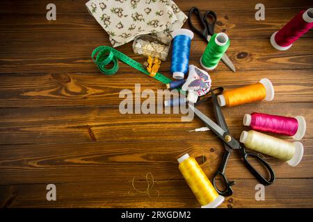 un ensemble d'outils et de fils pour coudre des vêtements, sur fond de bois. Banque D'Images