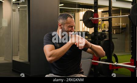 Homme afro-américain gars dans la salle de gym faisant des exercices de sport avec haltères entraînement athlète sportif soulevant des haltères lourds poids sentir la douleur vive dans Banque D'Images