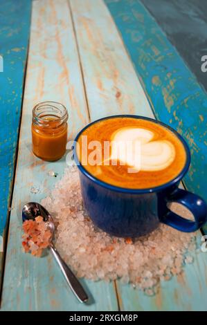 Mug cappuccino bleu avec caramel et anneau de sel de l'Himalaya en forme de coeur en mousse sur fond en bois bleu copie espace Banque D'Images