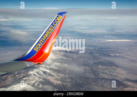 Une extrémité d'aile du Boeing 737 de Southwest Airlines survolant des montagnes enneigées. Les couleurs bleu et orange contrastent avec les sommets enneigés et le ciel clair. L'image capture l'esprit d'aventure de Southwest. Banque D'Images
