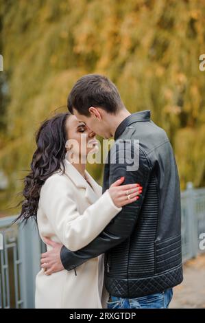 Un homme embrasse sa femme enceinte. Un homme dans une veste noire embrasse et embrasse une femme dans un manteau blanc. Automne Banque D'Images